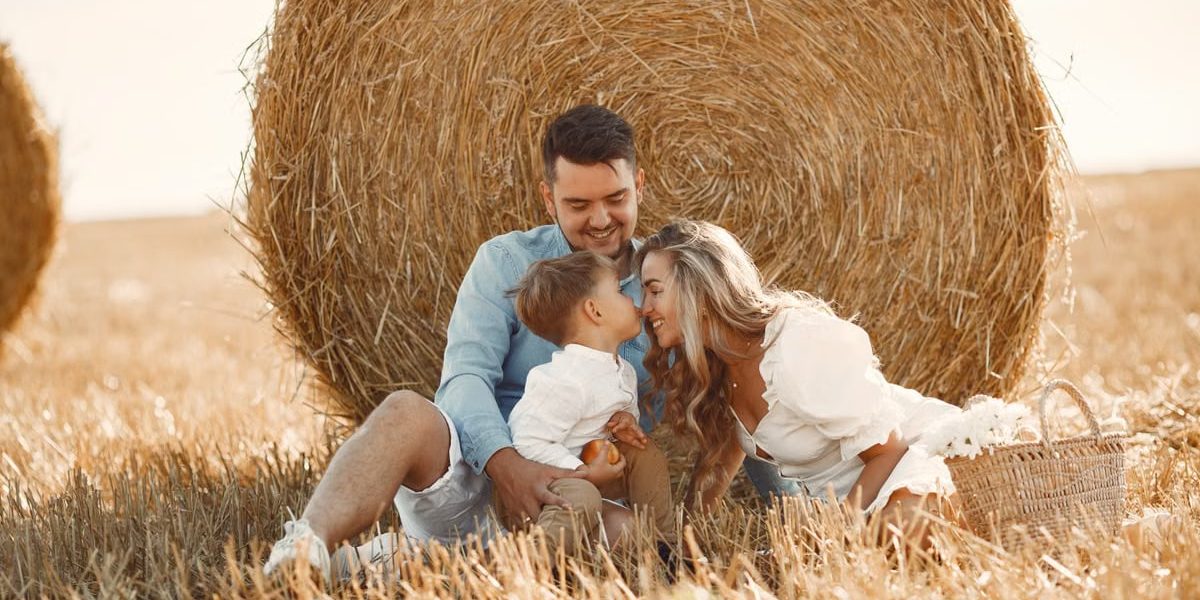 A happy family enjoying time together in a sunny, rural hay field, showcasing warmth and bonding.