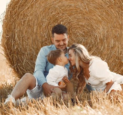 A happy family enjoying time together in a sunny, rural hay field, showcasing warmth and bonding.
