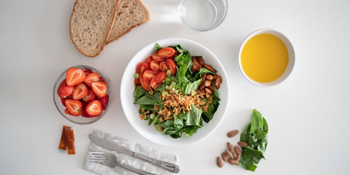 Top view of a healthy salad and fresh ingredients with bread and juice on a white surface.
