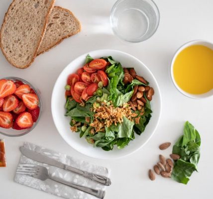 Top view of a healthy salad and fresh ingredients with bread and juice on a white surface.